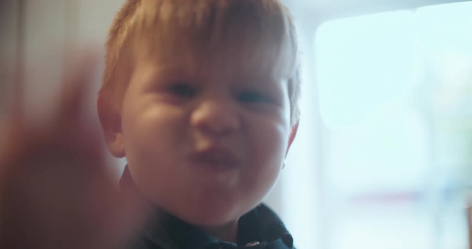 A charming little boy makes funny faces and waves at the camera in a slow-motion close-up
