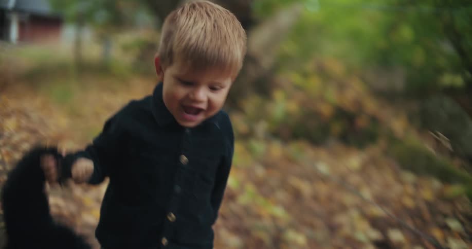 A joyful toddler with a big smile runs towards the camera in slow motion while holding his stuffed animal on an autumn path