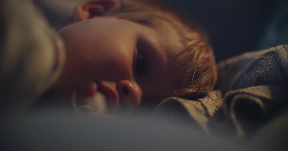 An intimate close-up of a peaceful baby with a pacifier as their eyes slowly close and they drift off to sleep