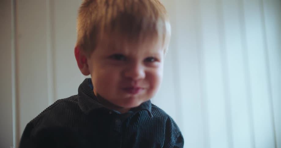 A young boy looks at the camera and makes a funny scrunchy face while eating in slow motion
