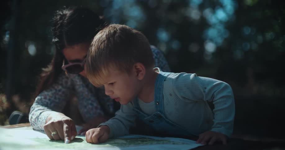 A mother and her young son lean over a trail map in a sunlit forest, pointing as they plan their adventure together