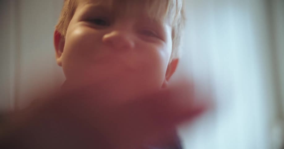 Close-up of a cute toddler looking into the camera, waving, and smiling with chubby cheeks in slow motion
