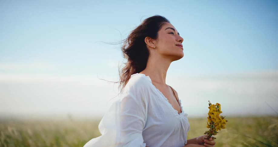 A beautiful woman enjoys a peaceful moment in a cinemagraph of a windy field, holding yellow flowers as the sun shines