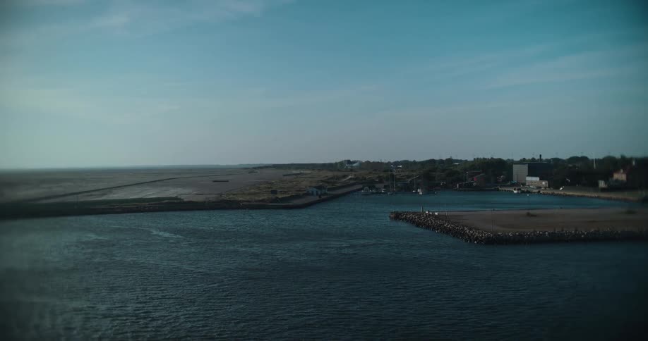 A peaceful wide shot of a small coastal harbor where the calm sea meets the land under a clear blue sky