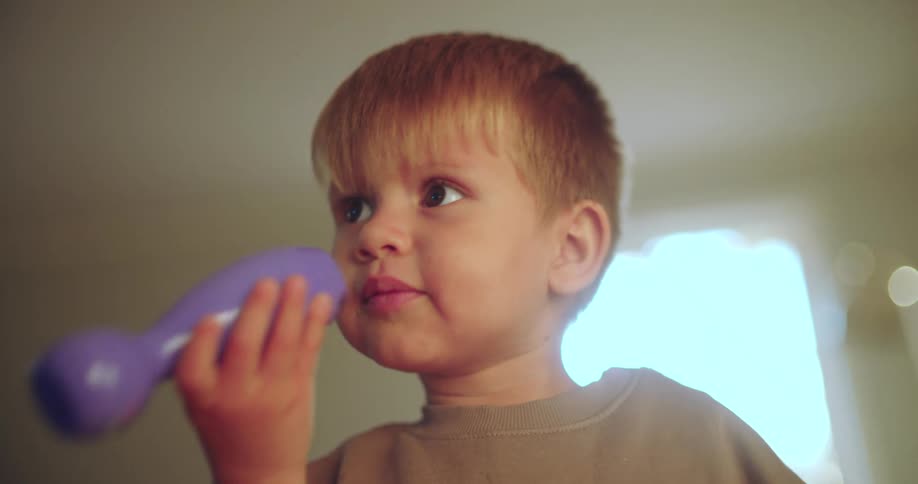 A cute toddler with chubby cheeks plays with a purple bowling pin toy in a warmly lit room