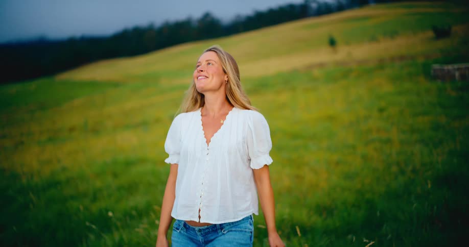 A serene pregnant woman walks through a beautiful green field, smiling peacefully as she connects with her baby