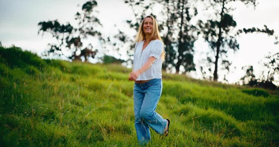 A beautiful and happy pregnant woman walks gracefully through a green grassy field, gently holding her belly
