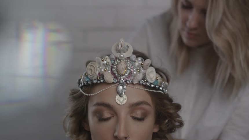 A woman wearing a crown has her hair made