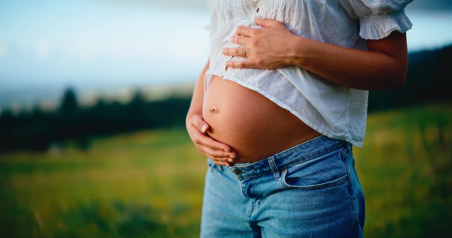 A peaceful cinemagraph shows a close-up of a pregnant woman gently holding her belly in a green field