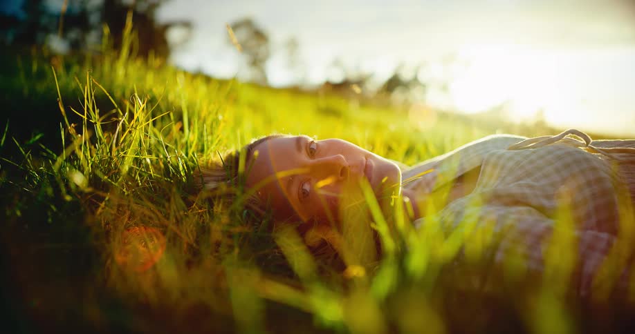 A peaceful woman closes her eyes and rests in a sun-drenched grassy meadow at sunset, embracing tranquility