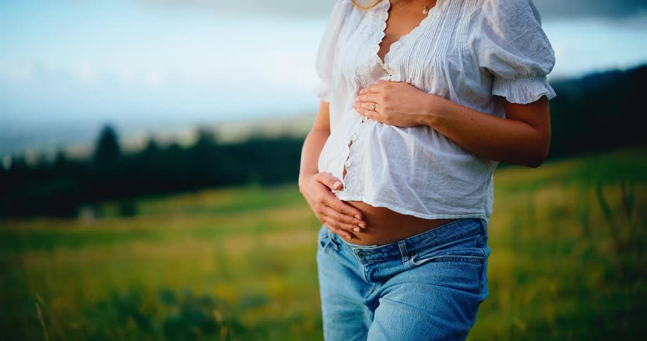 Serene close-up of a pregnant woman lovingly holding her baby bump while standing in a beautiful grassy field