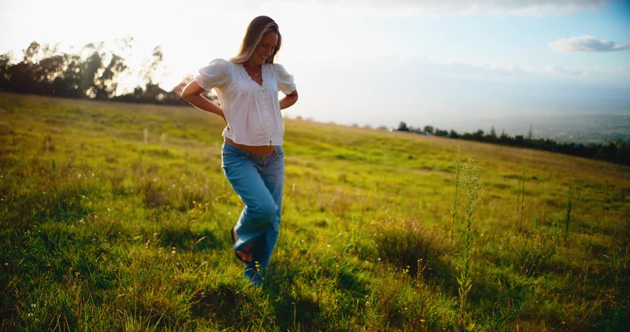 A smiling pregnant woman enjoys a peaceful walk through a beautiful green field at sunset
