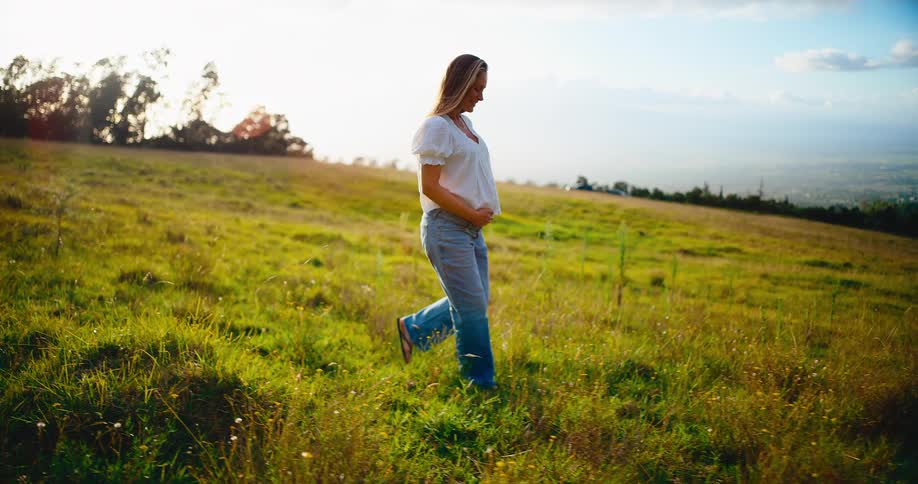 Happy and serene pregnant woman enjoys a peaceful walk through a beautiful grassy field during golden hour