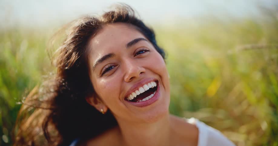 A beautiful young woman with a radiant smile laughs joyfully as the wind blows through her hair in a sunny field
