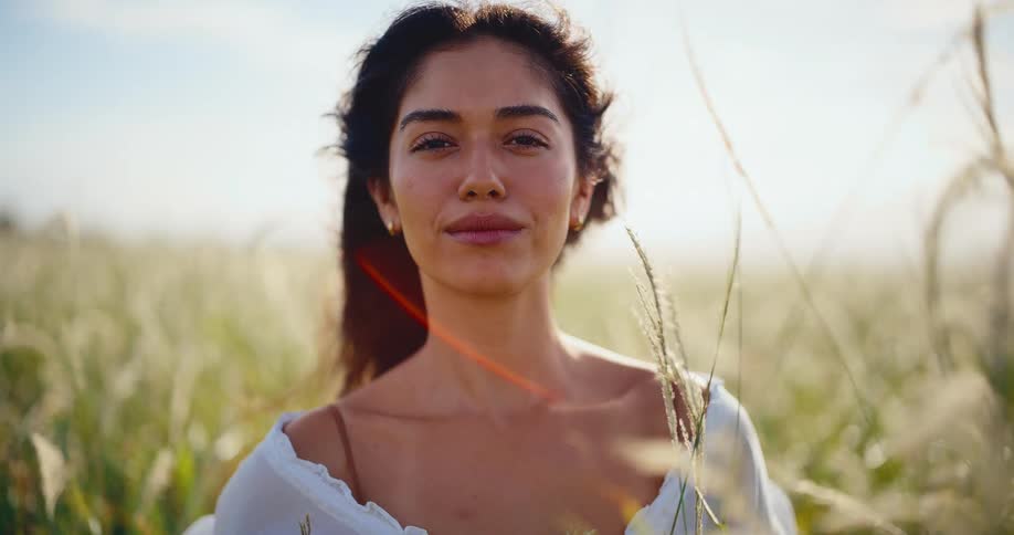 Portrait of a beautiful woman smiling peacefully in a sun-drenched field as the wind blows through her hair in slow motion
