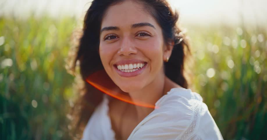 Joyful woman with a beautiful smile opens her eyes to the camera in a sun-drenched grassy field
