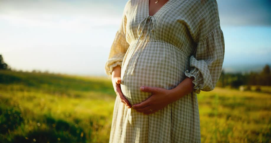 Cinemagraph of a pregnant woman holding her belly in a beautiful, sunlit grassy field