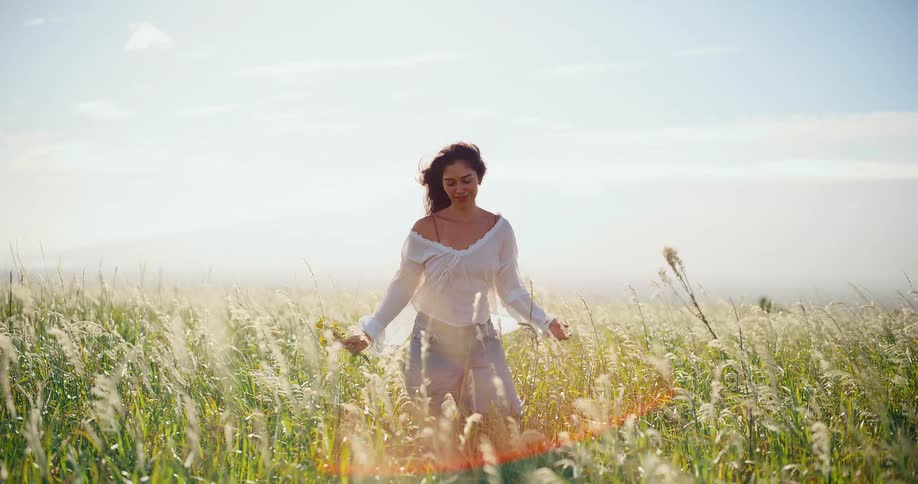 Slow motion of a happy and beautiful young woman walking peacefully through a field of tall grass in the afternoon sun