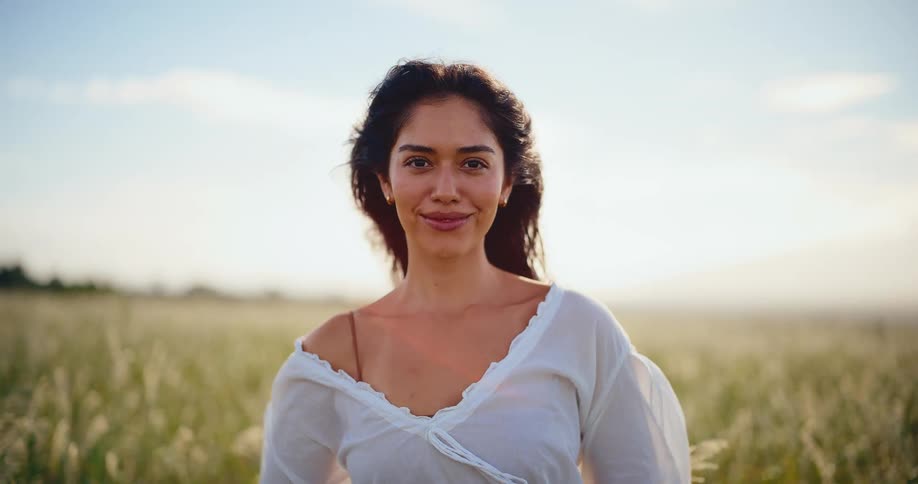 Serene portrait of a beautiful young woman enjoying the warm sunlight in a grassy field in slow motion