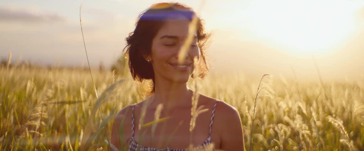 Serene portrait of a beautiful young woman smiling and enjoying the golden hour light in a breezy field of tall grass