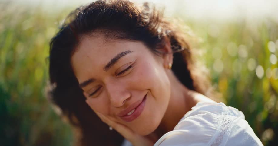 Serene close-up portrait of a beautiful young woman smiling gently in a sun-drenched field with a soft breeze in her hair