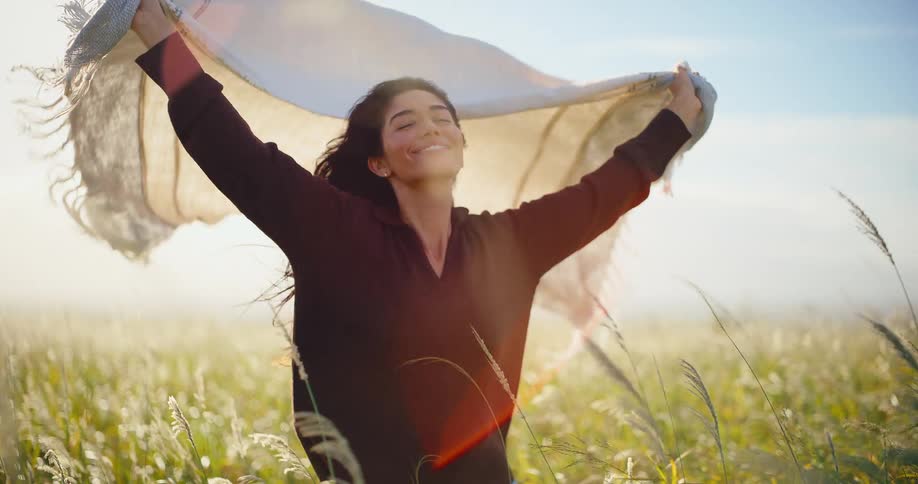 Slow motion shot of a happy woman holding a blanket in the wind while standing in a beautiful sunlit field