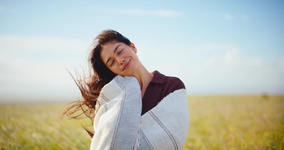 Serene portrait of a beautiful young woman wrapped in a cozy blanket, enjoying the warm sun and gentle breeze in a golden field