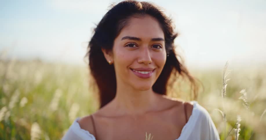 Portrait of a beautiful young woman smiling serenely in a sun-drenched field in slow motion