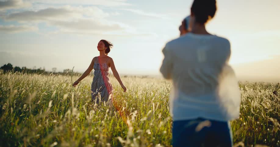 Woman photographs her friend modeling in a beautiful sunlit field during a golden hour photoshoot