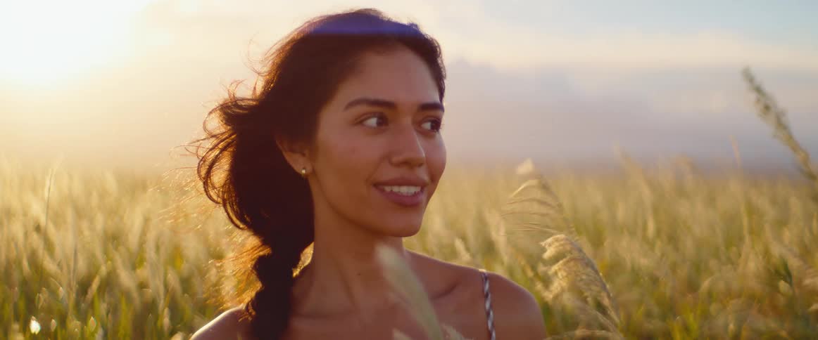 A beautiful young woman in a golden field smiles peacefully, enjoying the warm glow of sunset in slow motion