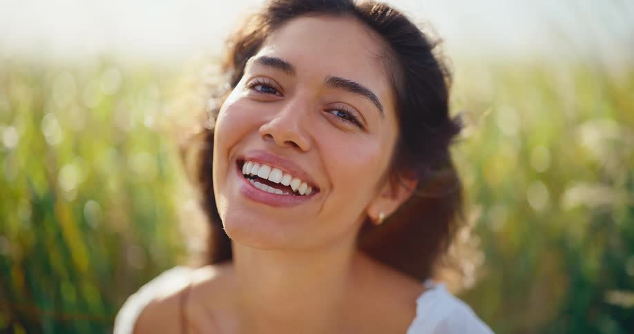 Slow motion portrait of a beautiful young woman with a radiant smile enjoying the sunshine in a grassy field