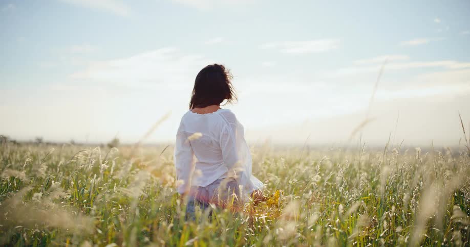 Beautiful woman holding a bouquet of yellow wildflowers wanders through a picturesque golden field in slow motion