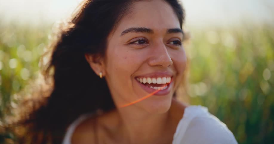 A beautiful young woman with dark curly hair laughs with pure joy in a sunlit field in slow motion