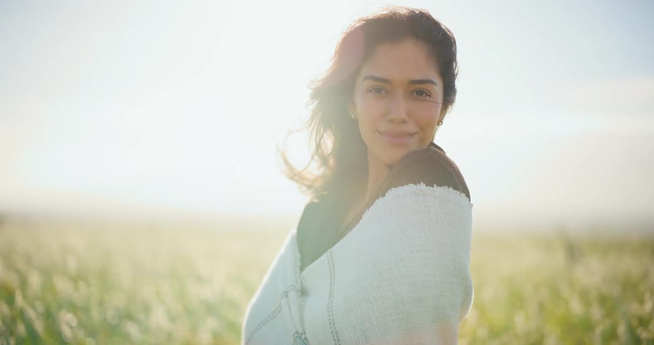 Serene woman wrapped in a blanket feels the warmth of the sun and gentle breeze in a beautiful golden field