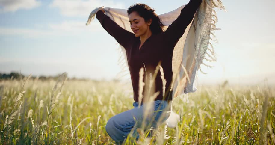 A carefree woman embraces the warm afternoon sun in a beautiful field of tall grass, holding a blanket in the wind