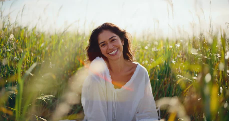 A beautiful happy woman smiles and laughs in a field of tall green grass at sunset in slow motion