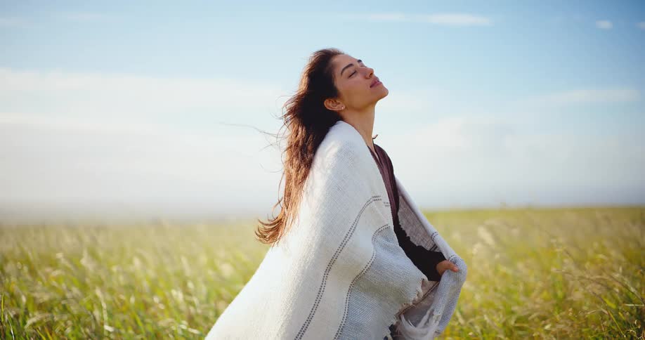 A beautiful young woman wrapped in a blanket enjoys the sun and wind in a golden field in slow motion