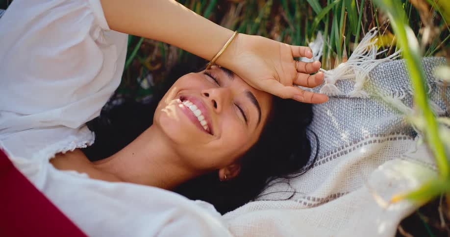 Close-up of a smiling young woman lying on a blanket in a field, basking in the warm sunlight