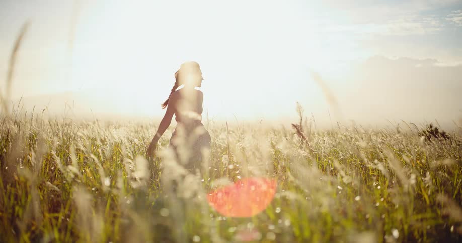 A beautiful young woman walks through a golden field of tall grass at sunset, enjoying her freedom in slow motion