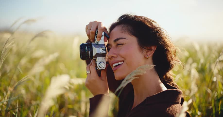 A beautiful young woman takes photos with a vintage camera in a sunny field, smiling peacefully