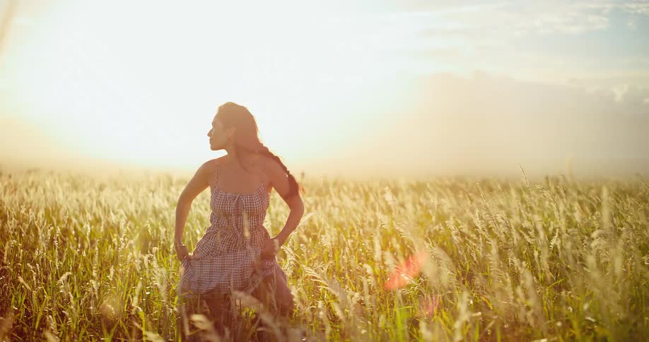A beautiful young woman runs through a sun-drenched golden field in slow motion at sunset, embodying a sense of freedom and joy