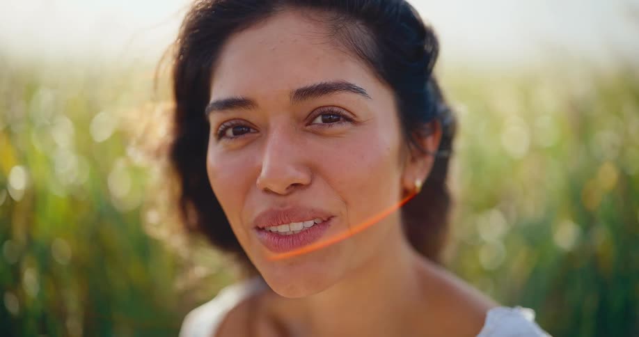Portrait of a beautiful young woman smiling happily and closing her eyes as she enjoys the warm sunlight in a green field