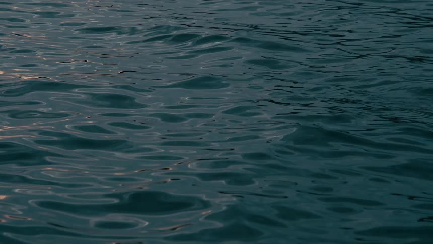 The surface of dark, tranquil water gently ripples in a mesmerizing slow-motion display