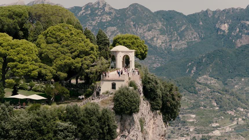 Guests mingle on the stunning Terrace of Infinity at Villa Cimbrone, perched on a cliffside in Ravello with a breathtaking view of the Amalfi Coast mountains