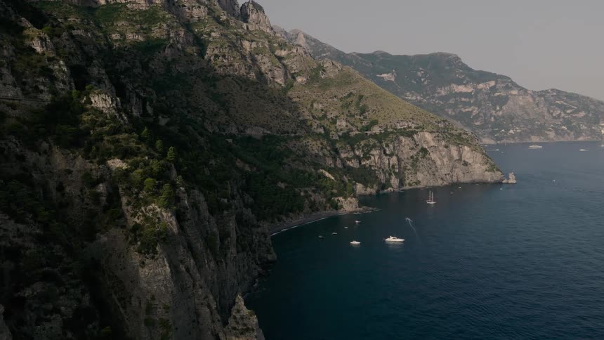 A majestic aerial view of the rocky Amalfi Coast in Italy, with numerous yachts and sailboats dotting the calm blue sea
