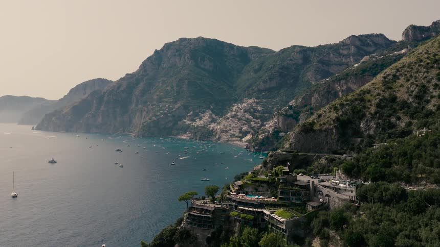 An expansive aerial shot slowly pushes towards the scenic Italian Amalfi Coast, showcasing its dramatic cliffs, blue waters, and distant seaside villages