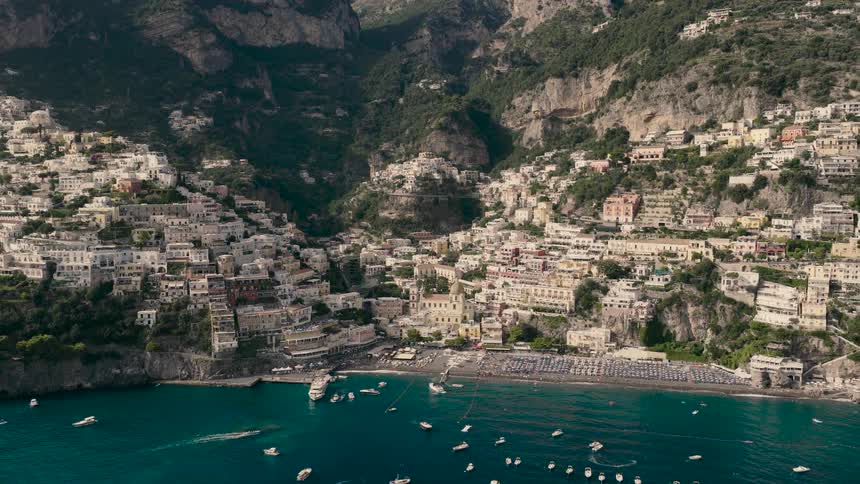 An epic aerial pullback reveals the iconic cliffside village of Positano on the Amalfi Coast, its busy beach, and the turquoise sea filled with boats