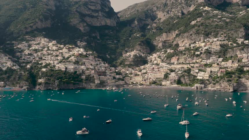 A stunning aerial view of the picturesque cliffside village of Positano on the Amalfi Coast, with many boats and yachts in the bay