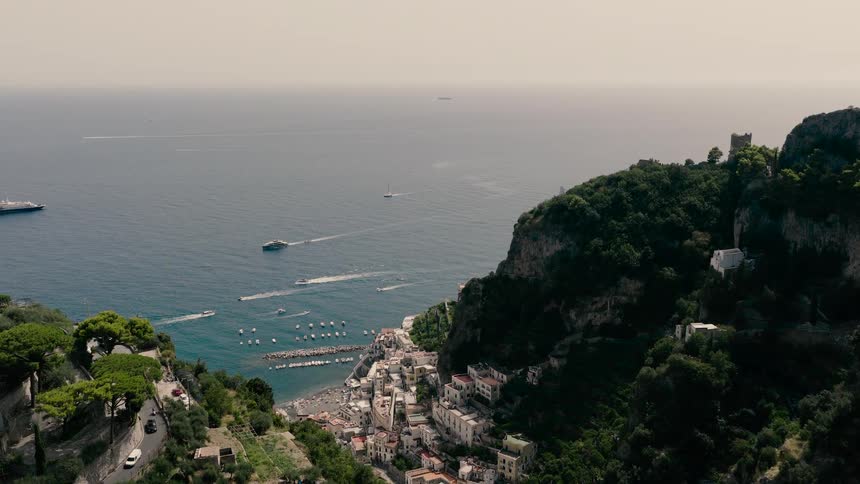 A stunning aerial view reveals the beautiful coastal town of Amalfi, nestled in a valley along the Italian coast, with boats dotting the turquoise sea