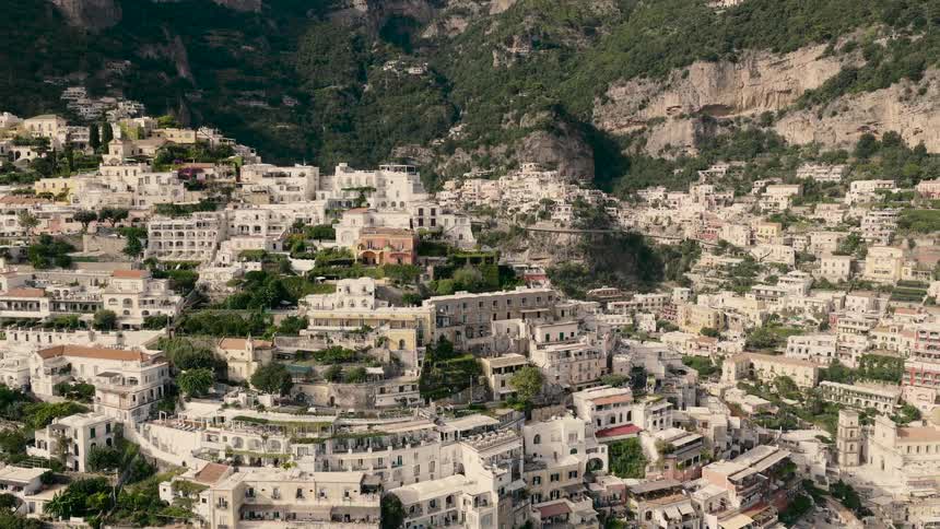 Slowly pulling back aerial shot reveals the beautiful, sun-drenched homes and hotels built into the cliffs of Positano, Italy